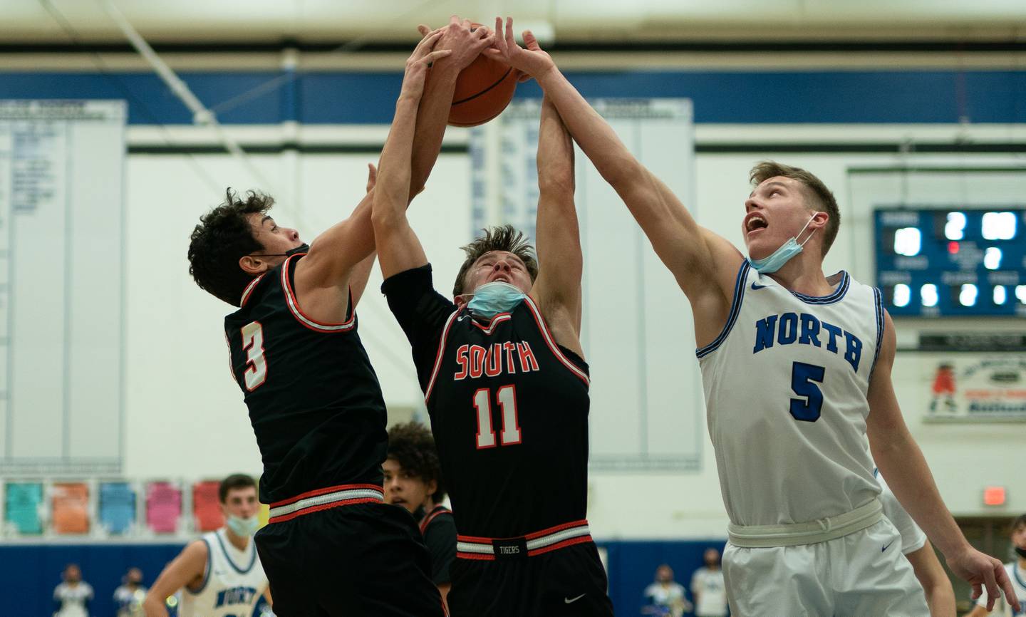 (Left to right) Wheaton Warrenville South's Rourke Robinson (3) Danny Healy (11) and St. Charles North's Jude Love (5) fight for a rebound during a basketball game at St. Charles North High School on Friday, Jan 21, 2022.