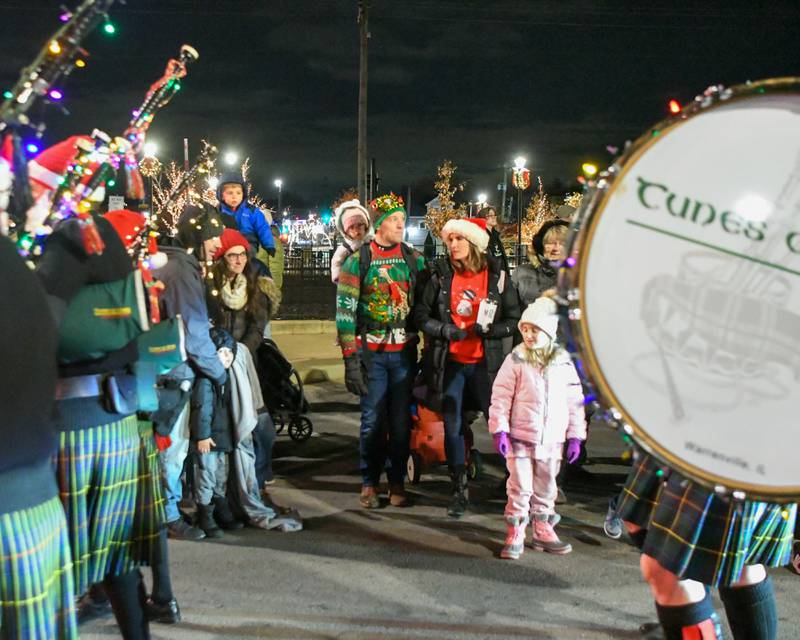 Family members Allan and Mackenzie Rovik, watch with their kids Everly Rovik, 2 years old, and Emery Rovik, 6 years old, of Wheaton as they watch as the Tunes of Glory bagpipes march by during the holiday parade in downtown Wheaton on Friday Nov. 24, 2023.