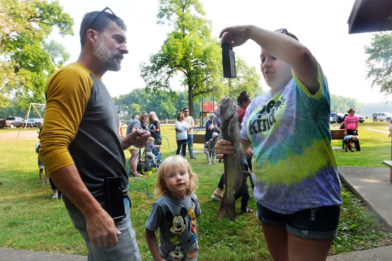 Ophelia Collinson, 3, of Tampico and her dad, Kelly, watch as Tara Gibson weighs the catfish she caught on her at the 17th Dick Brown Fishing Derby for kids at Prophetstown State Park on Saturday. The catfish weighed d3.5 pounds and the second fish caught.