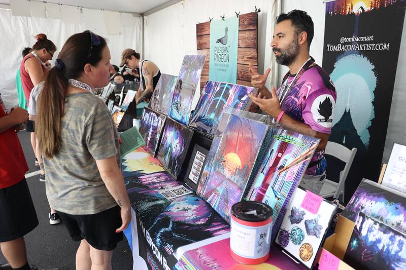 Roxane Potocki, left, talks with Tom Bacon, a Chicago-based artist, at his tent at Comicolopis, Lockport’s 7th annual Comic and Fandom Con on Saturday, July 29.