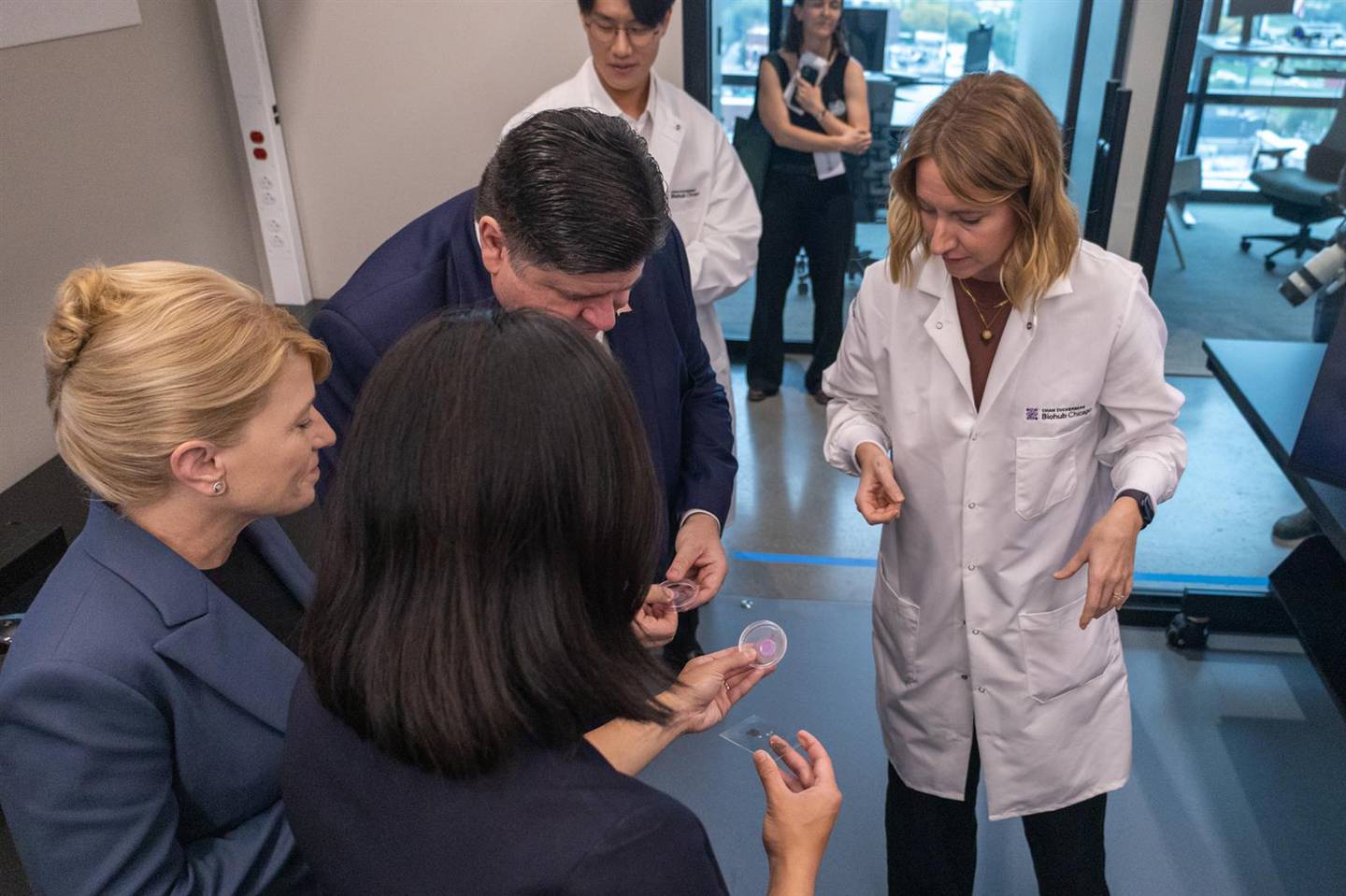 Gov. JB Pritzker, Chan Zuckerberg Biohub Chicago President Shana Kelley (left) and Chan Zuckerberg Initiative CEO Priscilla Chan huddle around tissue samples that are part of Biohub Fellow Hope Burks’ (right) research.