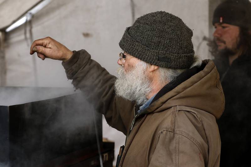 Chuck Howenstine warms his hand as he cooks down sap from maple trees on Thursday, March 9, 2023, at the Pioneer Tree Farm near McHenry. He has been collecting sap for most of his adult life to make maple syrup that he gives away.