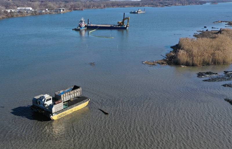 Workers use an amphibious dump truck (bottom) and barges with excavators (top) to haul silt near Delbridge Island about a mile east of the Starved Rock Lock and Dam on Tuesday, Feb. 13, 2024 near Starved Rock State Park. The Starved Rock Breakwater project is a habitat restoration effort designed to restore submerged aquatic vegetation in the Illinois River, Starved Rock Pool. It will increase the amount and quality of resting and feeding habitat for migratory waterfowl and improve spawning and nursery habitat for native fish.
Construction of the breakwater will involve placement of riprap along northern edge of the former Delbridge Island, adjacent to the navigation channel between River Mile 233 and 234. The breakwater structure will be approximately 6,100 feet long and constructed to a design elevation 461.85 feet, providing adequate protection to allow for submerged aquatic vegetation growth.
The estimated total cost of this project is between $5 and $10 million.