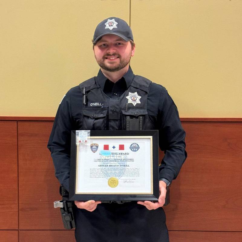 Montgomery Officer Bryan O'Neill stands with the Life Saving Award he was honored with at the May 13 Village Board Meeting for his courageous and selfless actions in saving an individual's life.