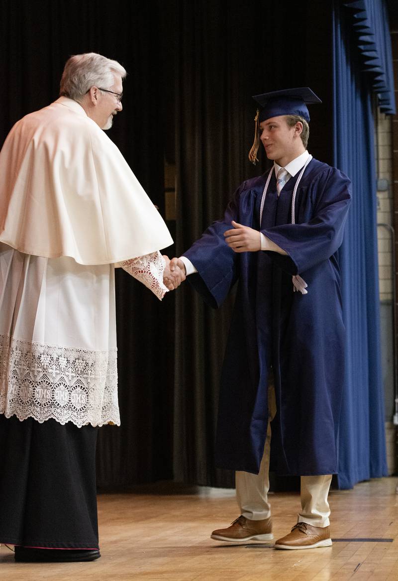 Peter McGrath shakes hands with the Rev. Monsignor Philip Halfacre just before receiving his diploma Sunday, May 26, 2024, during Marquette Academy High School's commencement ceremony.