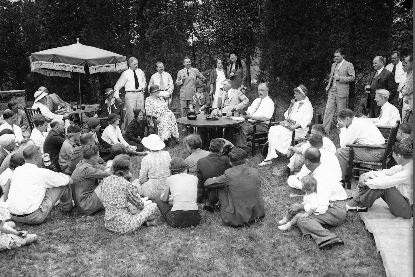 President Franklin Roosevelt reads to his guests as he and First Lady Eleanor Roosevelt, at table, host a Labor Day picnic at their residence in Hyde Park, N.Y., Sept. 3, 1934.