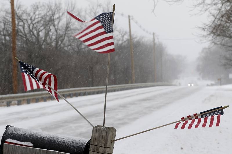 American flags whip in the wind as a car travels east on Main Street in Spring Grove on Thursday, Dec. 22, 2022, as a winter storm hits northern Illinois.