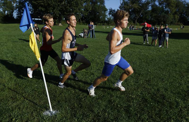 Woodstock’s Ellery Shutt, (right) Cary-Grove’s Jameson Tenopir (center) and Huntley’s Tommy Nitz (left) round a flag as they compete in the boys race of the McHenry County Cross Country Invite on Saturday, August 31, 2024, at McHenry Township Park in Johnsburg.