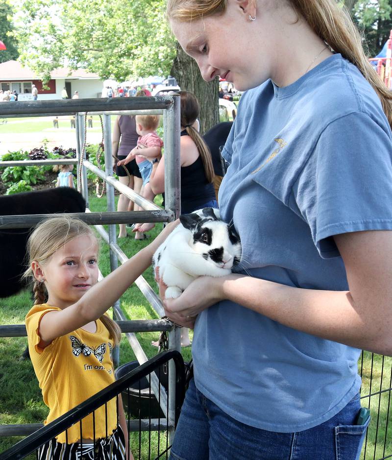 Summer Falkos, 8, from Paw Paw, pets a rabbit held by Allie Peterson, 16, from Shabbona, at the Indian Creek High School Future Farmers of America booth Saturday, July 15, 2023, at the Waterman Lions Summerfest and Antique Tractor and Truck Show at Waterman Lions Club Park.