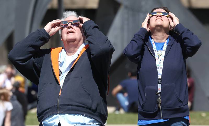 Pat McCarthy, from Sycamore, and Julie Polz, from Rochelle, both employees at Northern Illinois University, watch the eclipse Monday, April 8, 2024, at the NIU Solar Eclipse Viewing Party behind Davis Hall in DeKalb. Attendees were treated to perfect weather to watch the rare celestial event.
