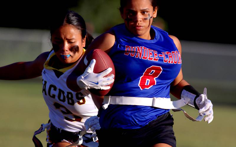 Dundee-Crown’s Skyler Noe, front, runs the ball as Jacobs’ Amy Trejo pursues the action in varsity flag football on Tuesday, Sept. 3, 2024, at Dundee-Crown High School in Carpentersville.