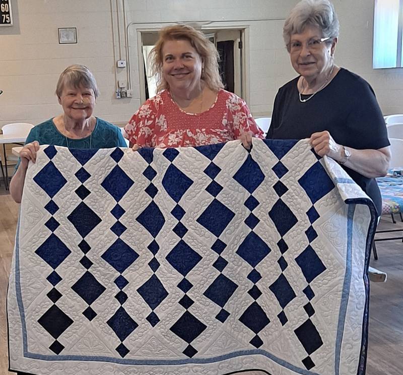 Sharon Di Prima, winner of the Quilters Dozen 2024 PrairieFest Quilt Raffle, picked up the quilt with her mother (from left), alongside Quilters Dozen President Diana Schlosser.