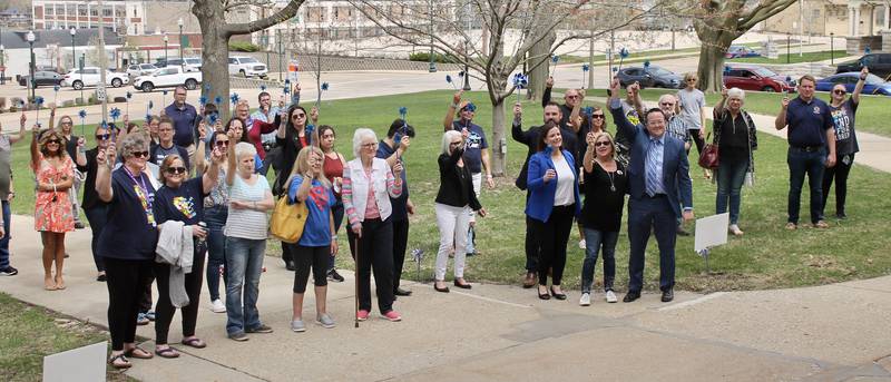 Participants in the Hands Around the Courthouse event as part of National Child Abuse Prevention Month hold aloft their blue pinwheels in a sign of solidarity on Friday, April 14, 2023, at the Old Lee County Courthouse in Dixon.