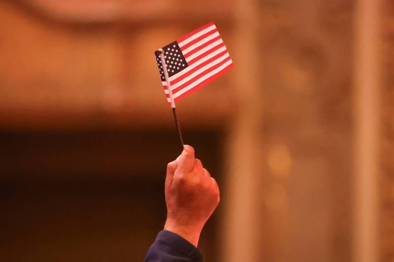 A newly appointed U.S. citizen waves an American flag after the Oath of Allegiance during the Special Naturalization Ceremony held at the Rialto Square Theatre in downtown Joliet on Tuesday, April 23, 2024.