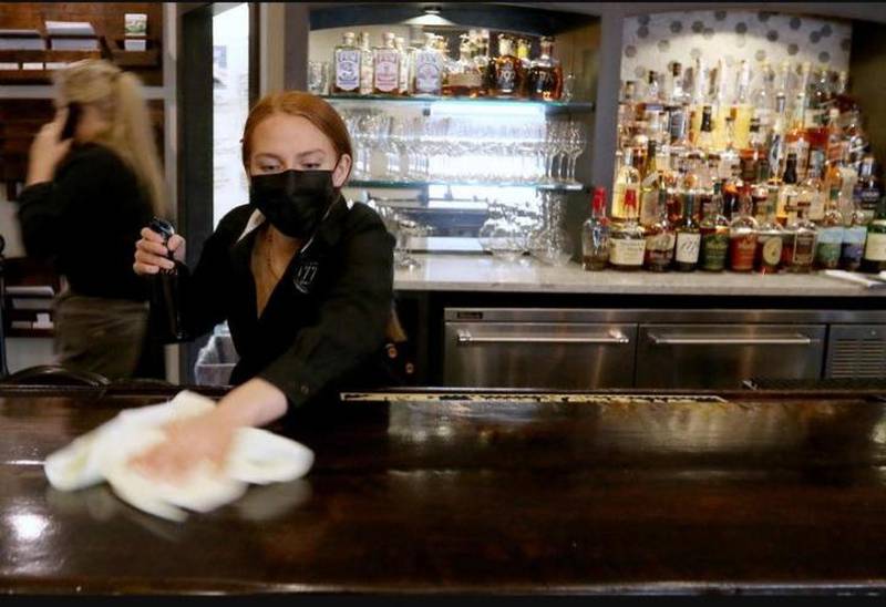 Bartender and server Brittany Crane prepares for the dinner rush Wednesday by performing cleaning tasks such as wiping down the bartop with a sanitizing solution at 1776 Restaurant in Crystal Lake. The restaurant is one of many local businesses that will have to adapt again to new COVID-19 safety guidelines in order to remain open for business.