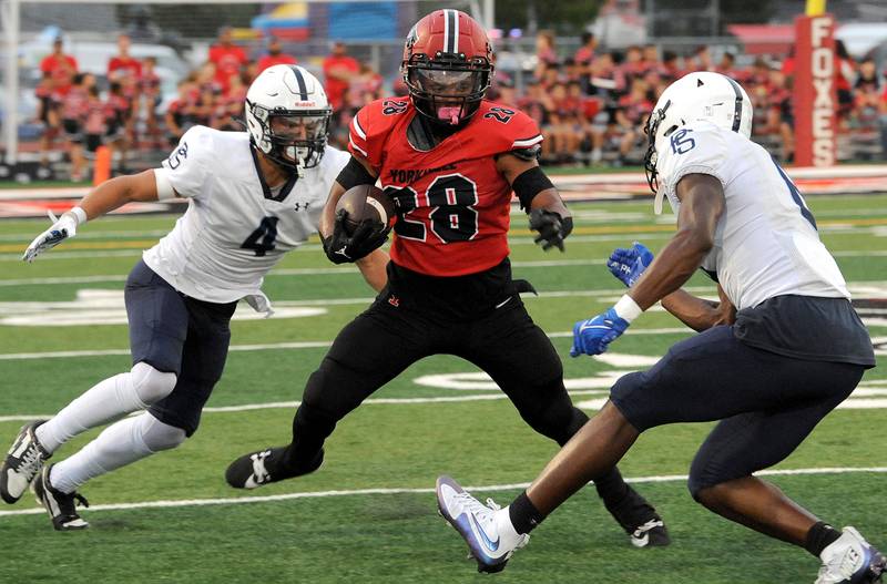 Yorkville running back T.J. Harland (28) tries to split Plainfield South defenders Chase Pierceall (4) and David Obadein on Friday, Sep. 30, 2024, at Yorkville High School.