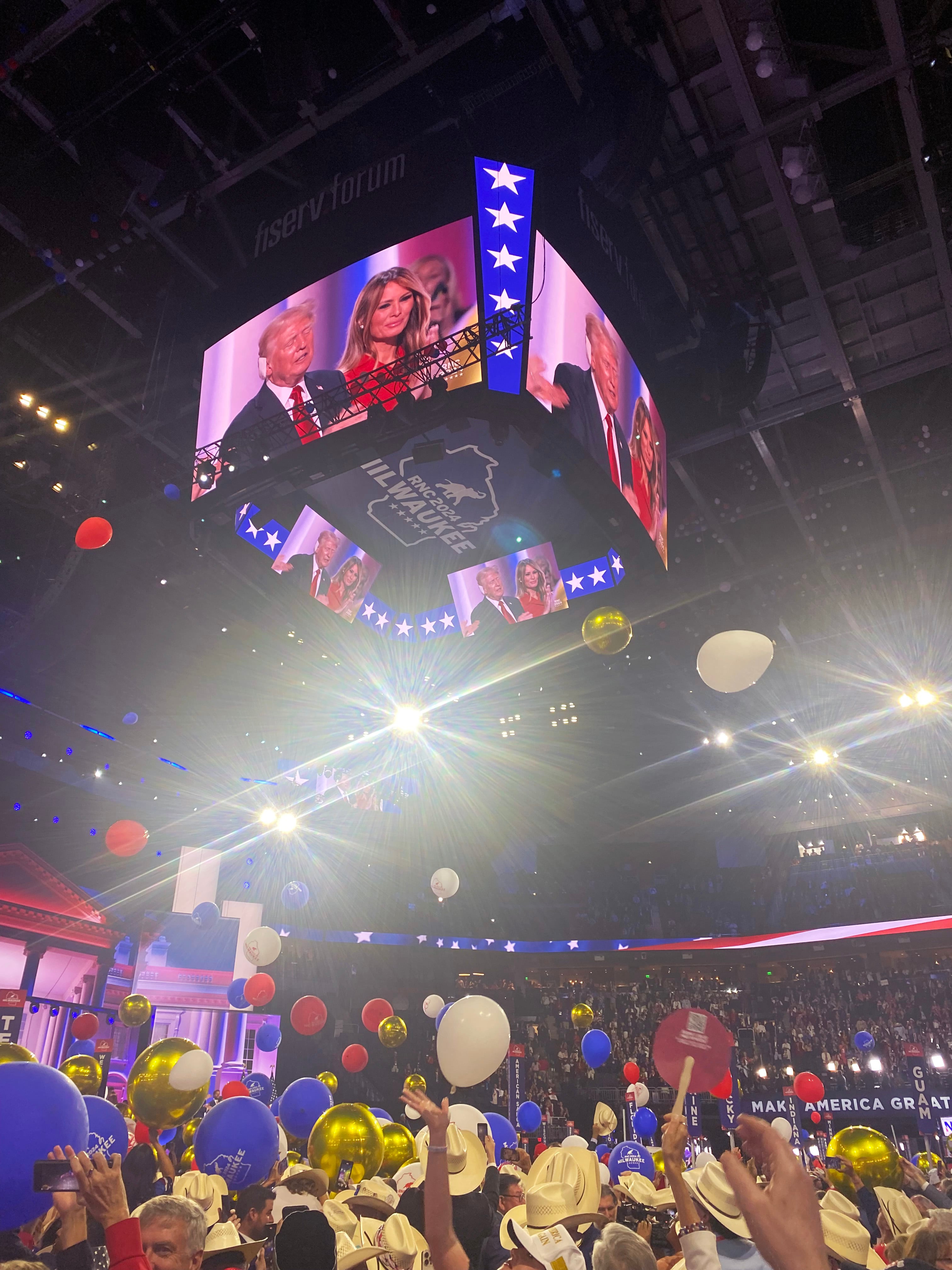 Attendees of the 2024 Republican National Convention cheer and balloons fall from the ceiling as former President Donald Trump and former First Lady Melania Trump are seen on a large screen on July 18, 2024.