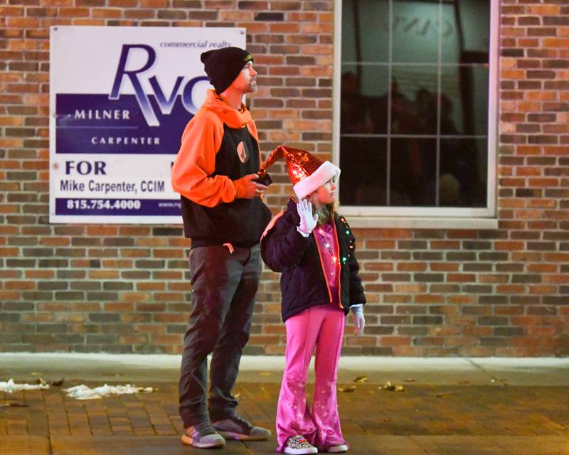 Steve Schweizer watches as daughter, Carolina Schweizer, 8, waves as Santa passes by Lincoln Highway during the DeKalb Chamber of Commerce's annual Lights on Lincoln and Santa Comes to Town event held in downtown DeKalb on Thursday, Nov. 30, 2023.