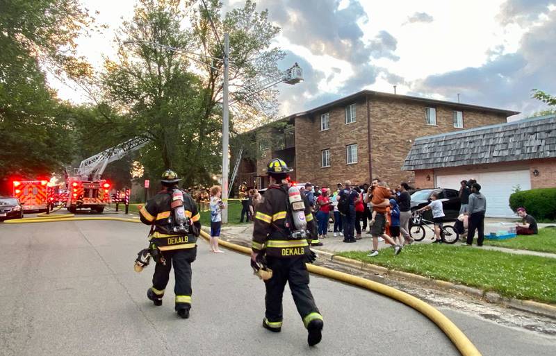 DeKalb firefighters head toward the staging area while evacuated residents look on at Kimberly Drive and Normal Road as authorities work to battle a structure fire at a Husky Ridge apartment complex in the 800 block of Kimberly Drive, DeKalb, on Wednesday evening, May 29, 2024.