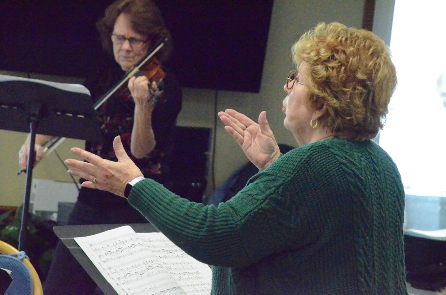 Sue Gilla of Montgomery, right, directs the Oswego Senior Singers at Wedgewood Manor in Montgomery on Dec. 16. Background is violinist Alyce Kuras of Sandwich.