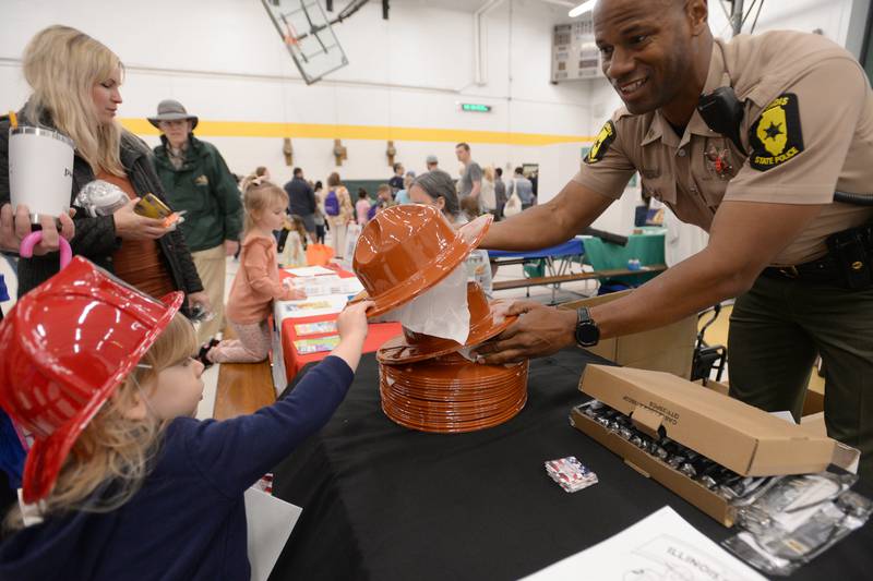 Children including Henry Legenza of Downers Grove receive hats from Illinois State Trooper Duane Chappell World of Reptiles employee Jeremy Taulbee during the Child Safety Expo held at Lakeview Junior High in Downers Grove Saturday June 1, 2024.